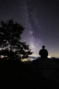 Rear view of silhouette man sitting against sky at night