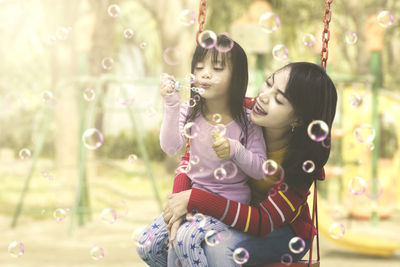 Mother and girl blowing bubbles at park