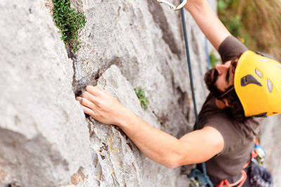 Sportive male alpinist climbing on sheer cliff in summer day