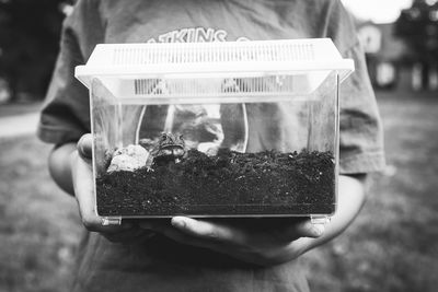 Midsection of boy holding toad in glass container on field