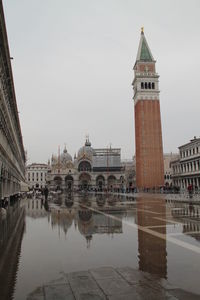 Reflection of tower on puddle in piazza san marco against sky