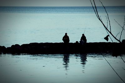 Silhouette men fishing in sea against sky