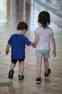 Rear view of cute sibling walking on tiled floor