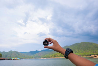 Cropped hand holding navigational compass by lake