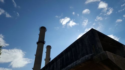 Low angle view of smoke stacks against cloudy sky