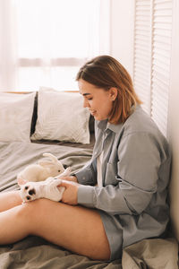 A cheerful young teenage woman plays with her pet a small dog in bed in the morning in a cozy house