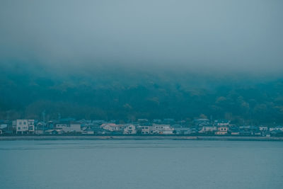 Buildings by sea in city against sky