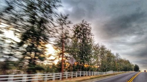 Road amidst trees against cloudy sky