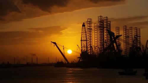 Silhouette of cranes at construction site during sunset