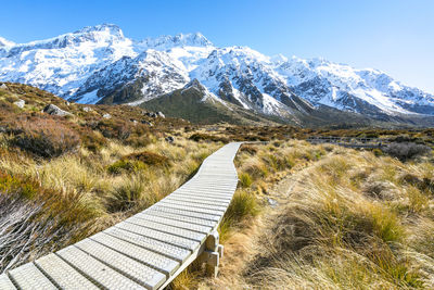 Narrow boardwalk leading towards snowcapped mountains