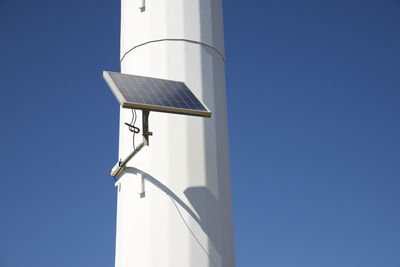 Low angle view of solar panel on windmill against clear blue sky