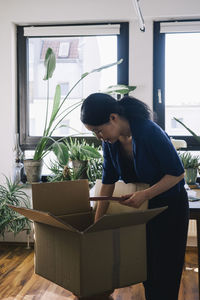 Mature female architect with plank and cardboard box at home office