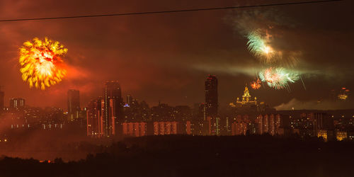 Firework display in city against sky at night