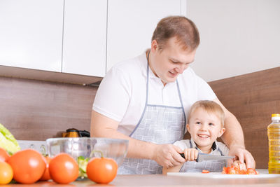 Happy family father with son preparing vegetable salad at home, vegetables