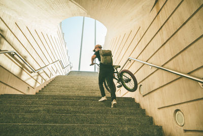 Low angle view of young man carrying bicycle while moving up on steps