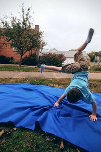 Full length of boy practicing handstand on blue fabric in back yard