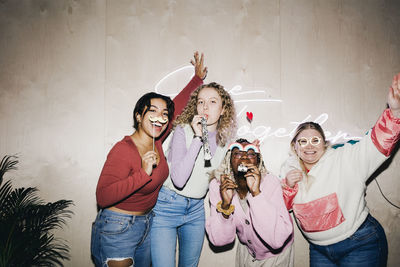 Portrait of happy multiracial female students with props against wall in college dorm