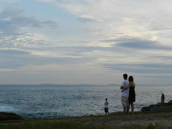 Rear view of couple standing at beach against sky