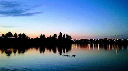 Silhouette swans swimming in lake against sky during sunset