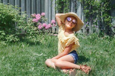 Stylish child girl in sunglasses and straw hat sitting on grass outdoor. happy smiling kid 