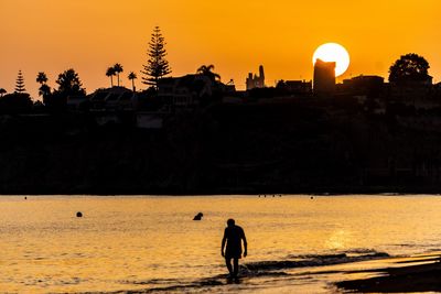 Silhouette man by sea against orange sky