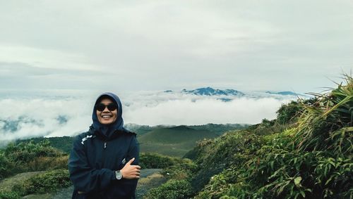 Portrait of smiling young woman in hoodie standing against landscape