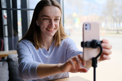 Young beautiful woman blogger making a video for her blog using phone camera in a cafe.