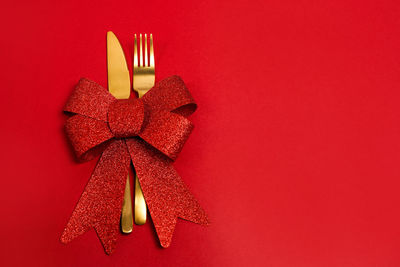 Christmas table place setting. golden fork and knife with red bow on red background, copy space