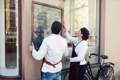 Male and female owners putting blackboard on wall outside grocery store