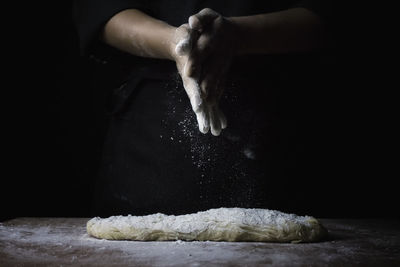 Midsection of chef preparing dough on table in darkroom