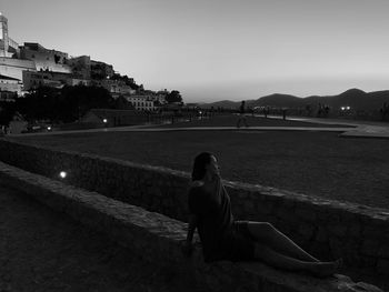 Rear view of woman sitting on land in city against sky at ibiza castle