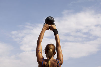 Rear view of woman with arms raised against sky