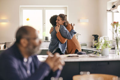 Smiling woman embracing mother-in-law while standing in kitchen at home