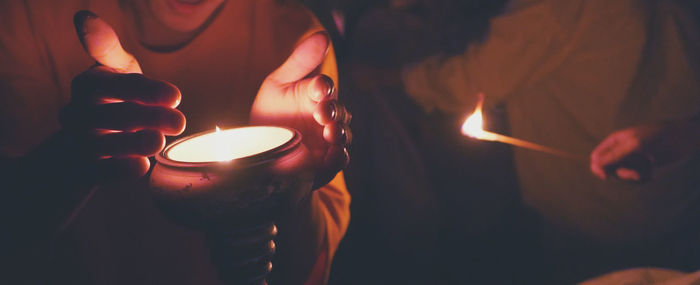 Close-up of hand by lit fire by person holding illuminated incense