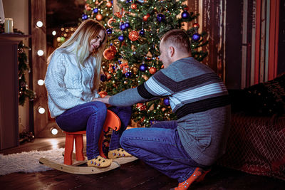 Rear view of woman sitting by christmas tree