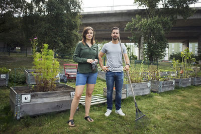 Full length portrait of mid adult couple with gardening tools at urban garden