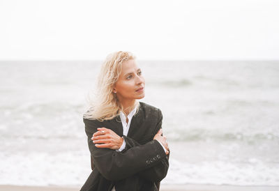 Portrait of elegant blonde woman in black suit near sea in a storm