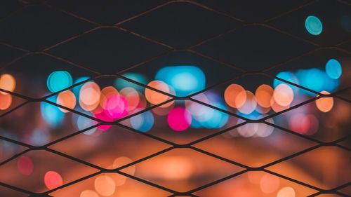 Full frame shot of defocused lights seen through chainlink fence