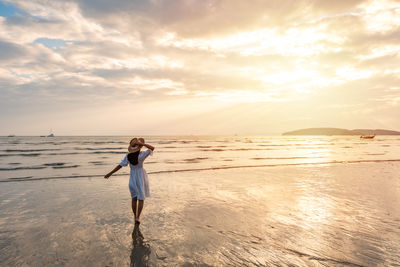 Rear view of man standing at beach against sky during sunset