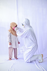 Full length of man wearing protective suit and mask to cute girl against white background