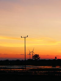 Silhouette electricity pylons on field against romantic sky at sunset