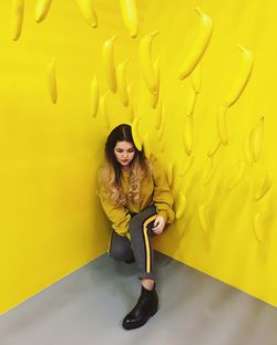 Woman in corner under artificial hanging bananas against yellow wall