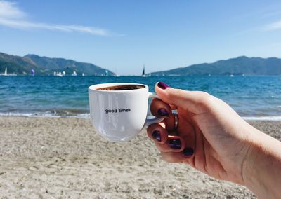 Midsection of man holding drink at beach against sky