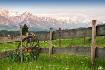 Wooden fence on field by mountains against sky