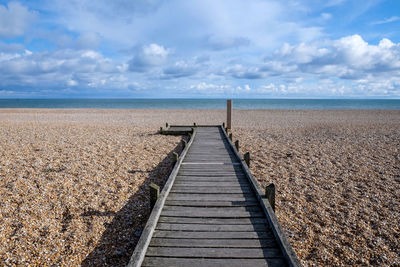 Boardwalk leading towards sea against sky