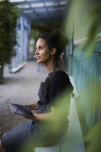 Thoughtful female gardener holding tablet computer in shade