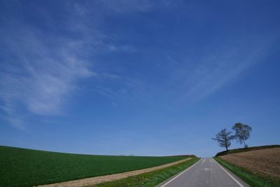 Empty road by field against sky