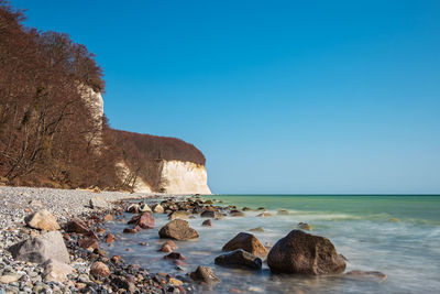 Rocks on beach against clear blue sky