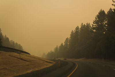 Road by trees against clear sky during sunset