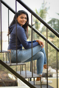Portrait of young woman sitting on railing